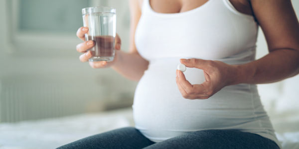 A pregnant person holding a glass of water and a white pill.