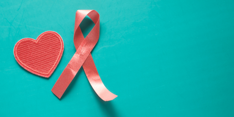 Red heart and red ribbon symbolising HIV awareness on a teal background